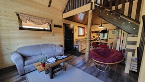 Un intérieur de chalet chaleureux avec un canapé, une table basse en bois, un fauteuil suspendu et un escalier.