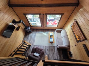 A cozy cabin interior with a sofa, a chair, a wooden table, a television, and a fireplace.