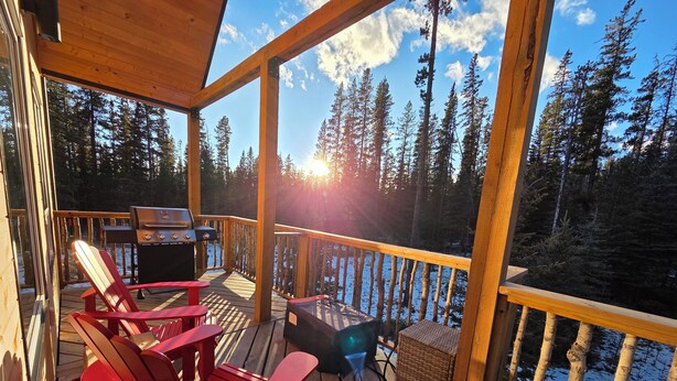 Une terrasse en bois avec des fauteuils Adirondack rouges, un barbecue et un panier en osier.