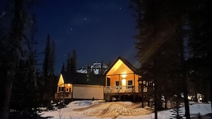 Un chalet au revêtement extérieur en bois et doté d’un balcon, entouré de neige et d’arbres, avec une montagne en arrière-plan.