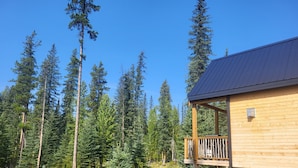 Une cabane en bois dotée d’un balcon, entourée de grands pins et surplombant un ciel bleu azur.