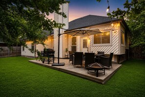 A covered patio with outdoor furniture, a fire pit, and string lights.