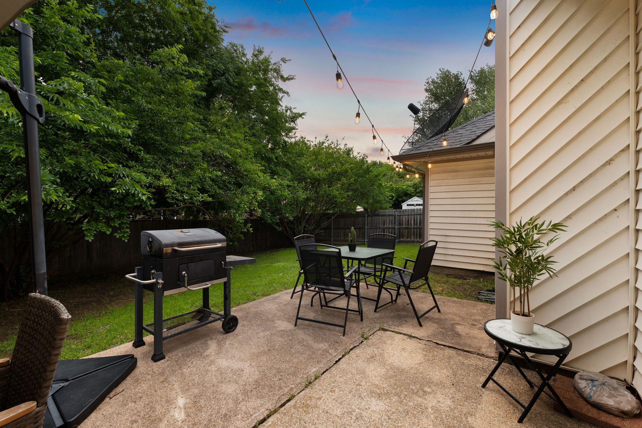 Une terrasse à l’arrière de la maison, avec un barbecue, une table et des chaises d’extérieur, et une plante en pot.