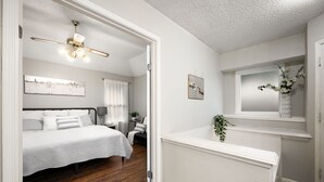 Ein Schlafzimmer mit Bett, Deckenventilator, Nachttisch und Fenster mit Pflanze.