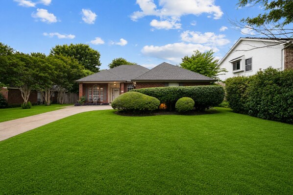 A residential house with a well-maintained lawn, a driveway, and a brick exterior.