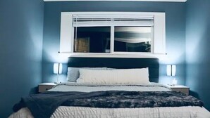 Quarto com uma cama, duas mesas de cabeceira, uma janela com persianas e luminárias na parede.
