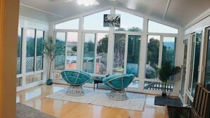 Uma sala de sol com grandes janelas, duas cadeiras, um ventilador de teto e vista para o exterior.