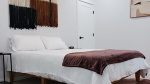 Un dormitori amb un llit, una taula de nit, una obra d'art penjada a la paret, una porta i un ventilador de sostre.
