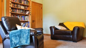 A living room with a leather armchair, a sofa, and a wooden bookshelf filled with books. - 1 bedroom accommodation in Llanfynydd (Llanfynydd)