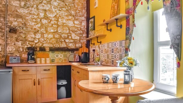 A kitchen with stone wall backsplash, wooden cabinets, and a round wooden table. - 1 bedroom accommodation in Llanfynydd (Llanfynydd)