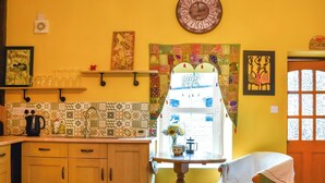 A kitchen with wooden cabinets, a sink, and a window with a view. There is a clock on the wall and a chair with a blanket. - 1 bedroom accommodation in Llanfynydd (Llanfynydd)