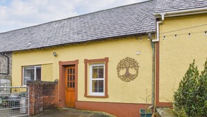 A yellow building with a tiled roof, a wooden door, and a window with a tree design. - 1 bedroom accommodation in Llanfynydd (Llanfynydd)