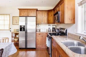 Una cocina con gabinetes de madera, un refrigerador de acero inoxidable, un microondas, una estufa y un lavamanos doble.
