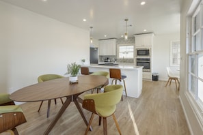 A modern kitchen with white cabinets, a central island, and a dining area with a round table and chairs.