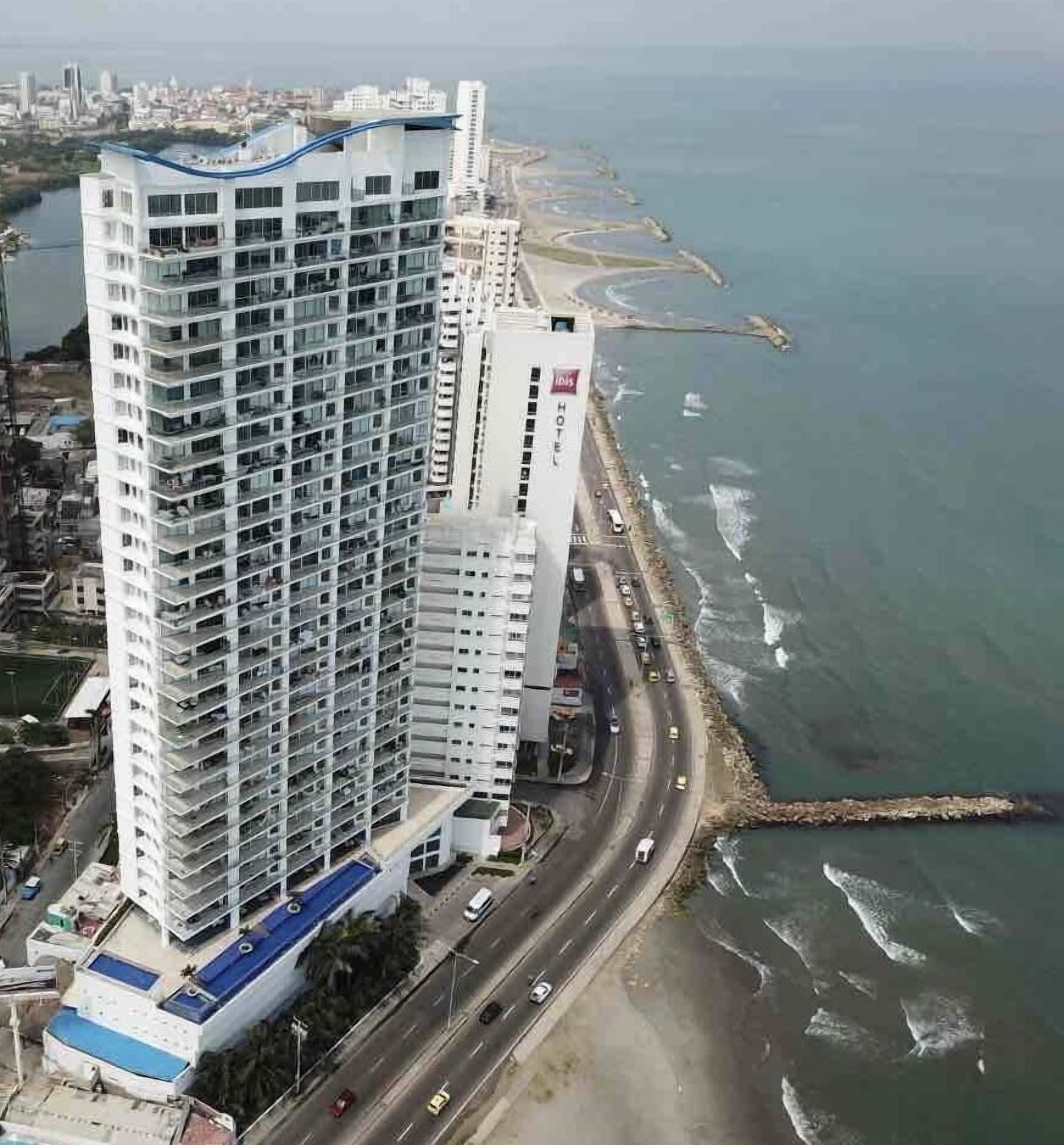 A high-rise hotel with multiple floors, a blue rooftop, and a view of the sea.