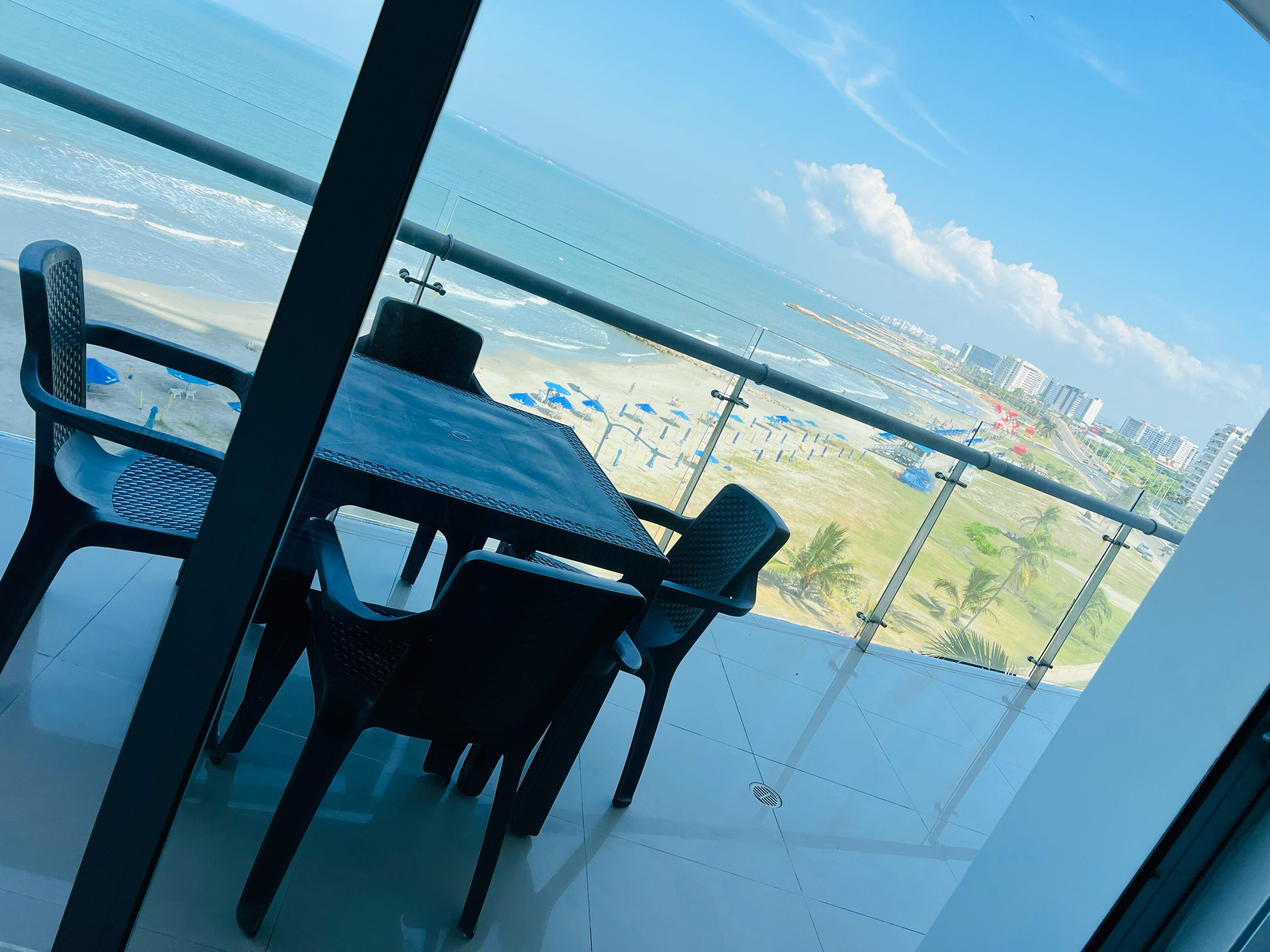 A balcony with a table and chairs, overlooking a beach and cityscape.