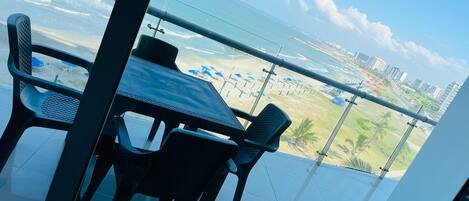 A balcony with a table and chairs, overlooking a beach and cityscape.
