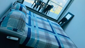 A hotel room with a large window, a bed with a patterned bedspread, a bedside table with a remote control, and a view of the outdoors. - Apartamento frente al mar Cartagena (Cartagena)