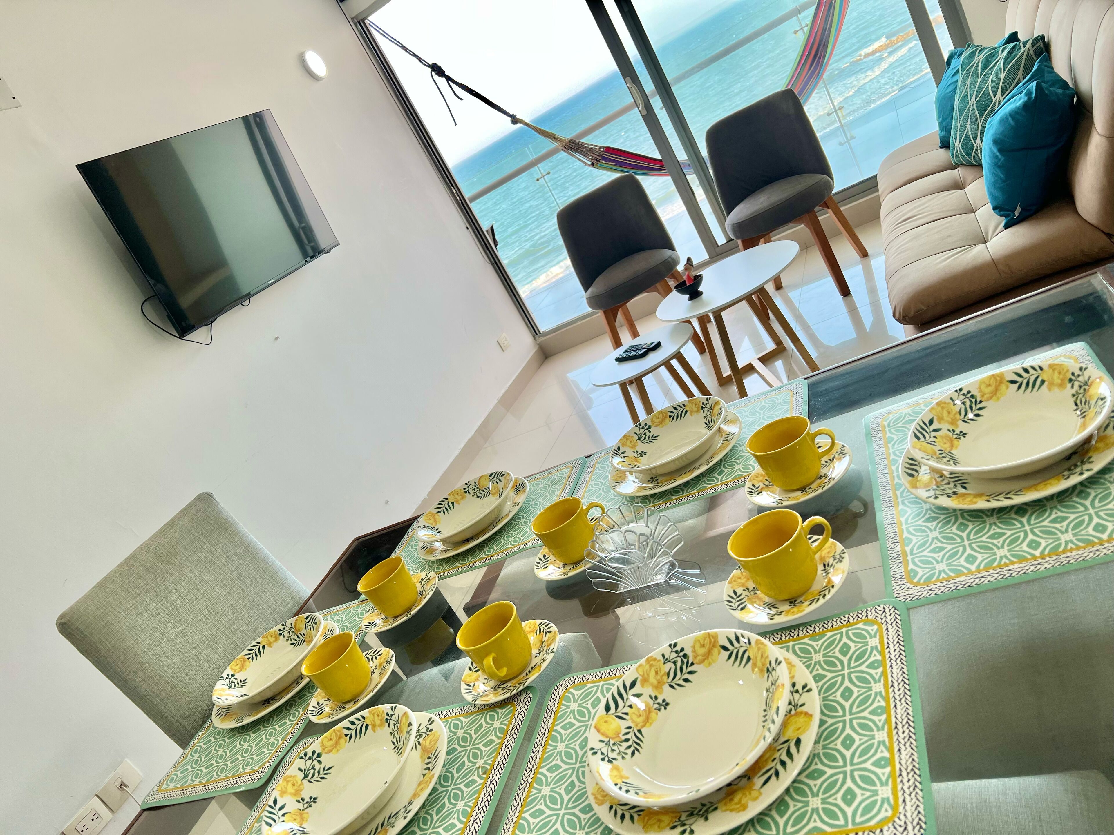 A dining area with a table set for four, featuring yellow and green floral plates and cups.