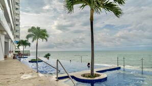 A swimming pool with palm trees, a view of the sea, and a building with balconies. - Apartamento frente al mar Cartagena (Cartagena)