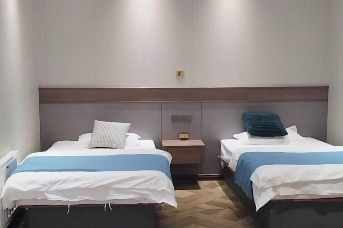 Habitación de hotel con dos camas, una mesita de noche y suelo de madera.