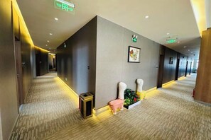 A hotel corridor with a carpeted floor, a bench, a small table, and a wall-mounted plant.
