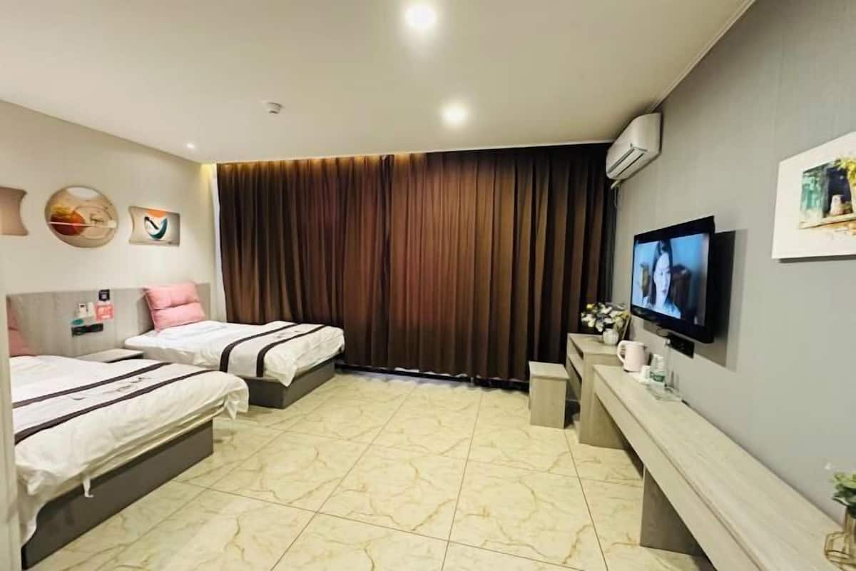 Habitación de hotel con dos camas, televisor, escritorio y un ventanal grande con cortinas.