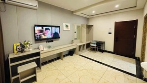 A modern hotel room with a flat-screen TV mounted on the wall, a wooden console table, a bench, and a small table with a chair. - Greater Khingan Tahe Chengxin Business Hotel (Tahe)