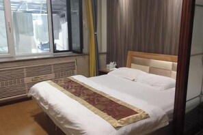 A hotel room with a large bed, a window with blinds, a bedside table, and a radiator. - Greater Khingan Tahe Chengxin Business Hotel (Tahe)