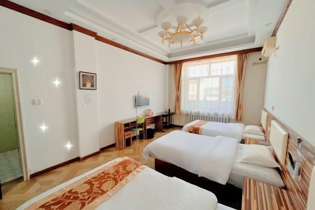A hotel room with two beds, a desk, a chair, a television, and a window with curtains.