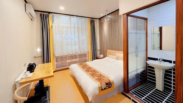 A hotel room with a bed, bedside table, and a bathroom with a sink and mirror. - Greater Khingan Tahe Chengxin Business Hotel (Tahe)