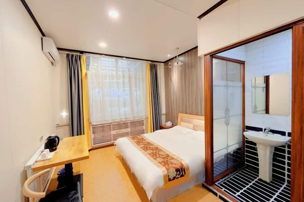 Habitación de hotel con cama, mesita de noche y baño con lavabo y espejo.