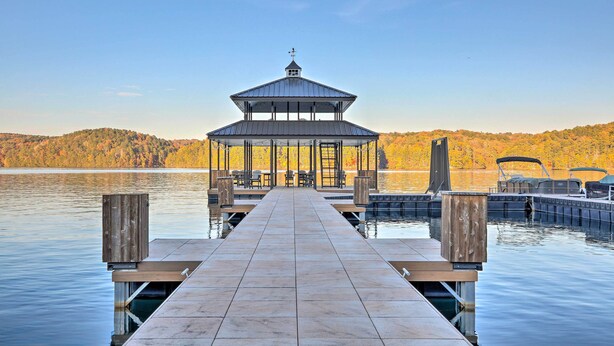 A wooden dock leading to a gazebo with a metal roof, overlooking a calm lake with autumn-colored trees in the background. - Lake Access: Waleska House w/ Floating Dock! (Waleska)