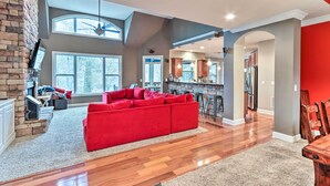 A spacious living area with a red sectional sofa, a fireplace, and a kitchen in the background. - Lake Access: Waleska House w/ Floating Dock! (Waleska)