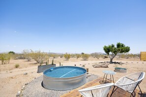 A hot tub with two chairs and a tree in a desert landscape.