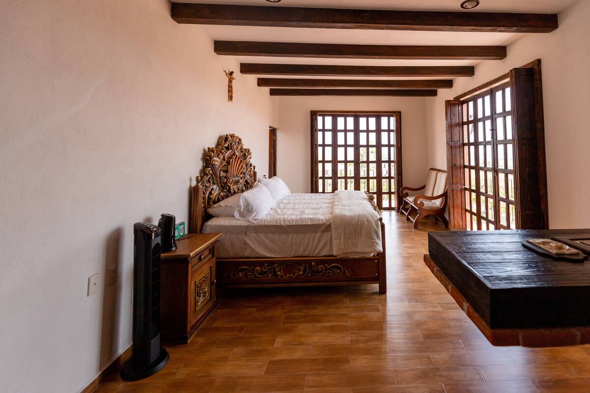 Un dormitorio con una cama de madera, una mesita de noche, un aparador y un ventanal con vistas.