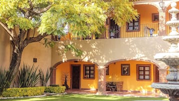 A courtyard with a fountain, a tree, and a building with arches and a balcony.