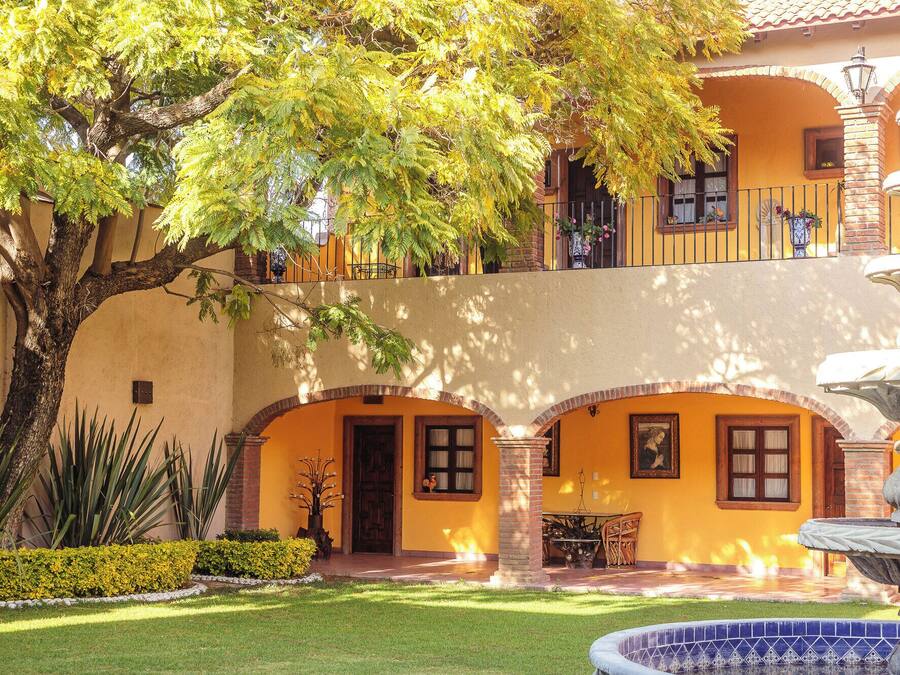 A courtyard with a fountain, a tree, and a building with arches and a balcony.