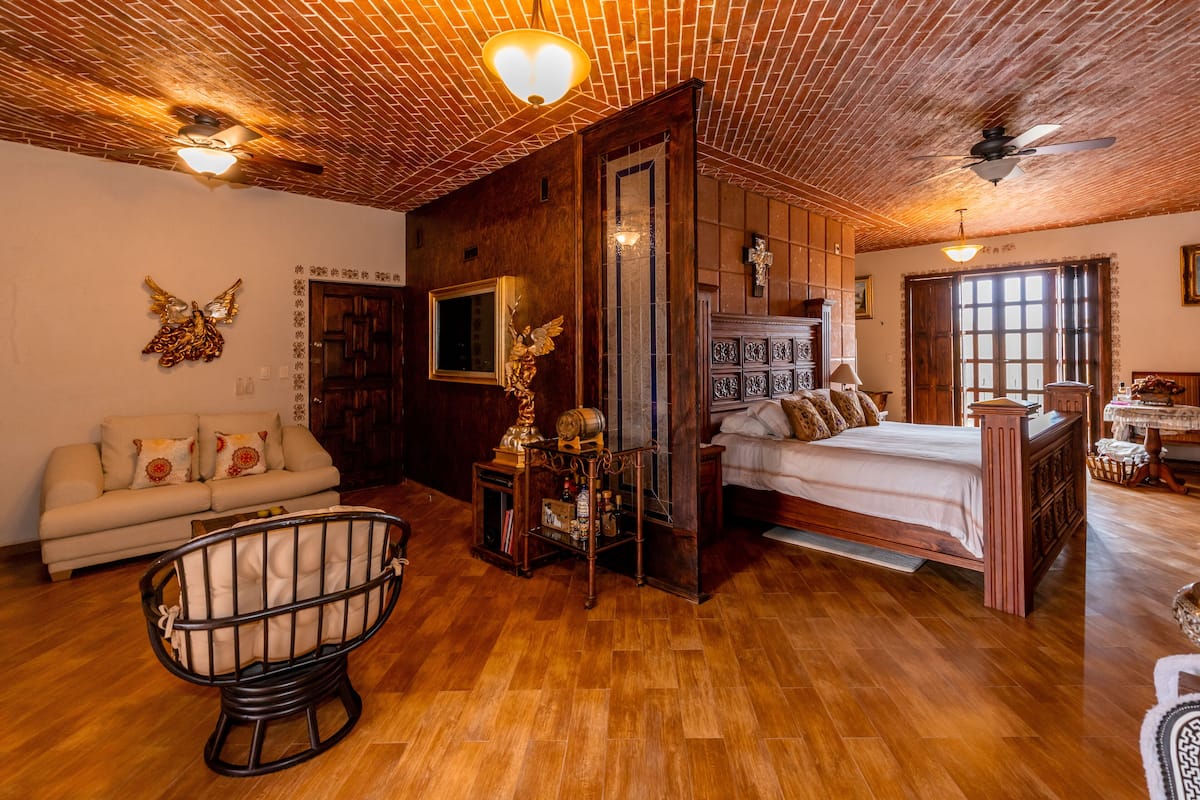 Una habitación acogedora con techo de madera, una cama, un sofá y un sillón mecedora.