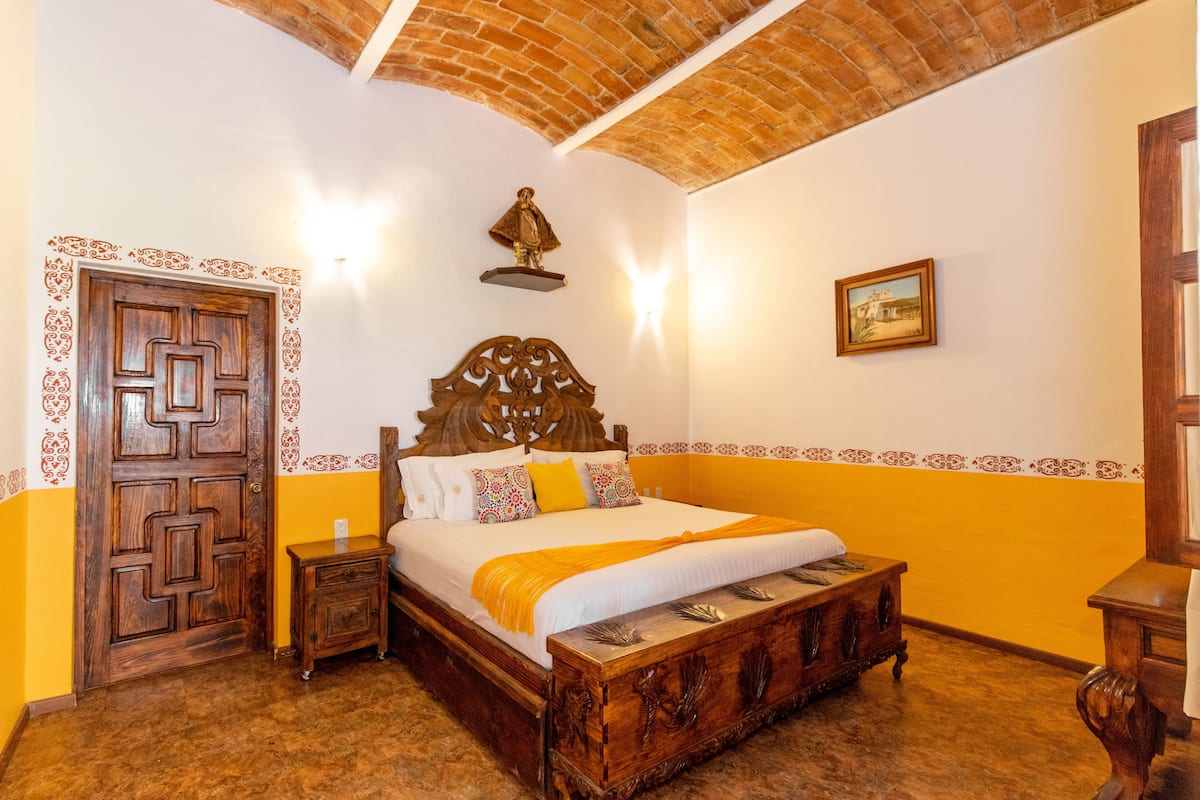 Una habitación con una cama de madera, una mesita de noche, una lámpara de pared y una puerta con diseño geométrico.