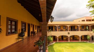 Un patio con suelo de baldosas, un corredor cubierto y un edificio con varios balcones y ventanas.