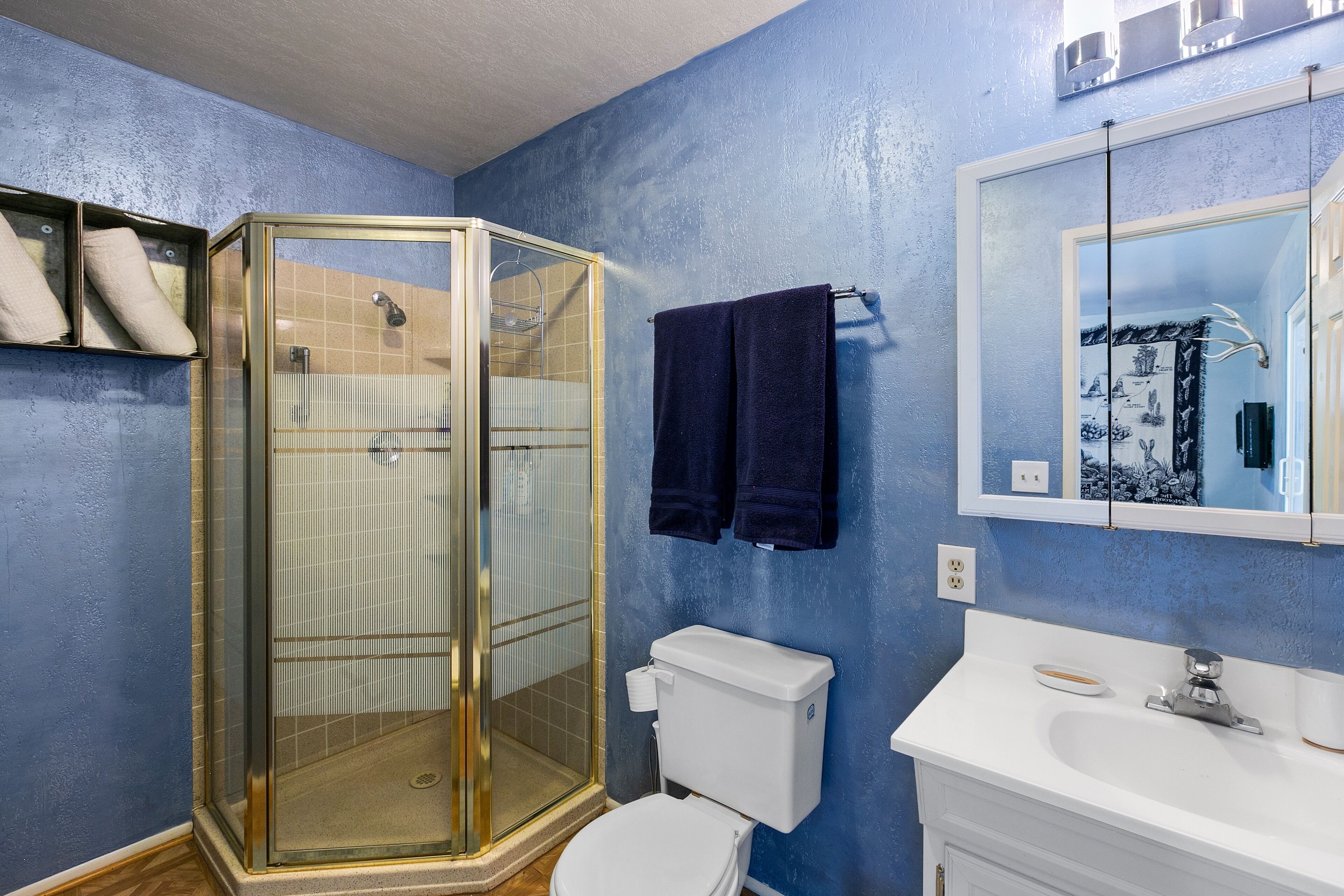 A bathroom with a glass-enclosed shower, a toilet, a sink, and a mirror.