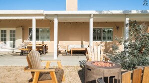 An outdoor patio area with wooden furniture, a hammock, and a fire pit. - Hillside Desert House - Hot Tub, Fire Pit And Bbq! 3 Bedroom Home by RedAwning (Yucca Valley)