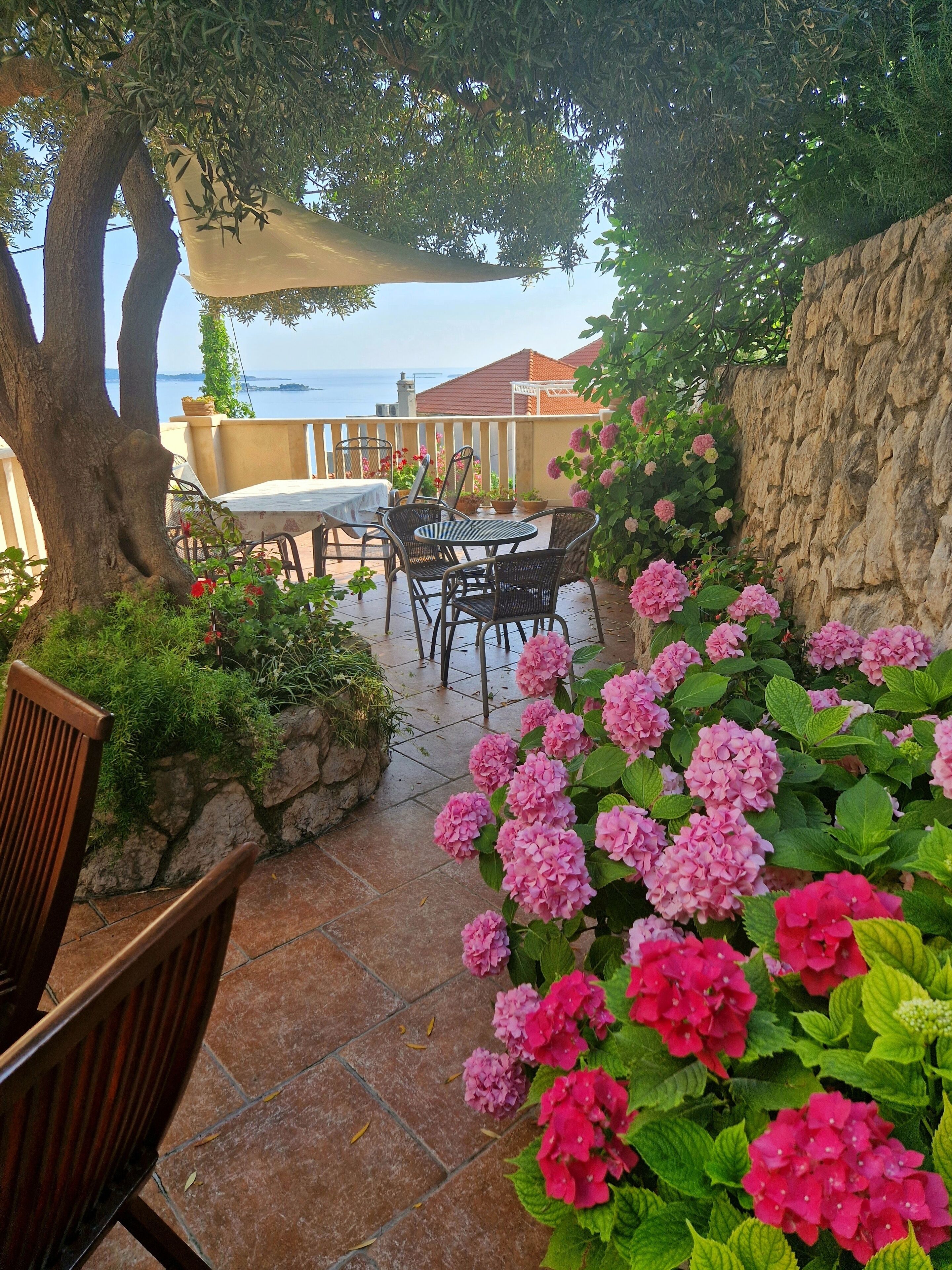 An outdoor patio with a table and chairs, surrounded by potted plants and flowers.