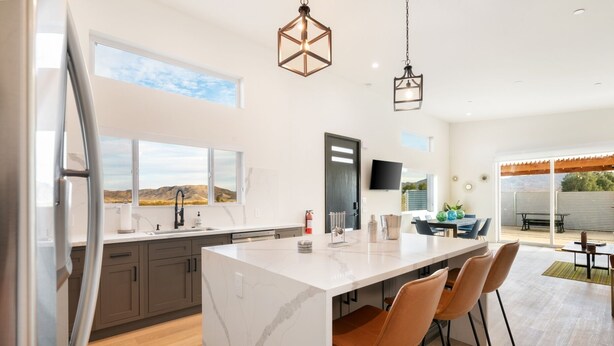 A modern kitchen with a large island, dark cabinets, and a view of the desert. - Sun Oro Joshua Tree - Hot Tub, Bbq, Fire Pit & Gameroom 2 Bedroom Home by RedAwning (Joshua Tree)