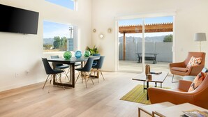 A modern living room with a dining area, large windows, and a view of mountains. - Sun Oro Joshua Tree - Hot Tub, Bbq, Fire Pit & Gameroom 2 Bedroom Home by RedAwning (Joshua Tree)