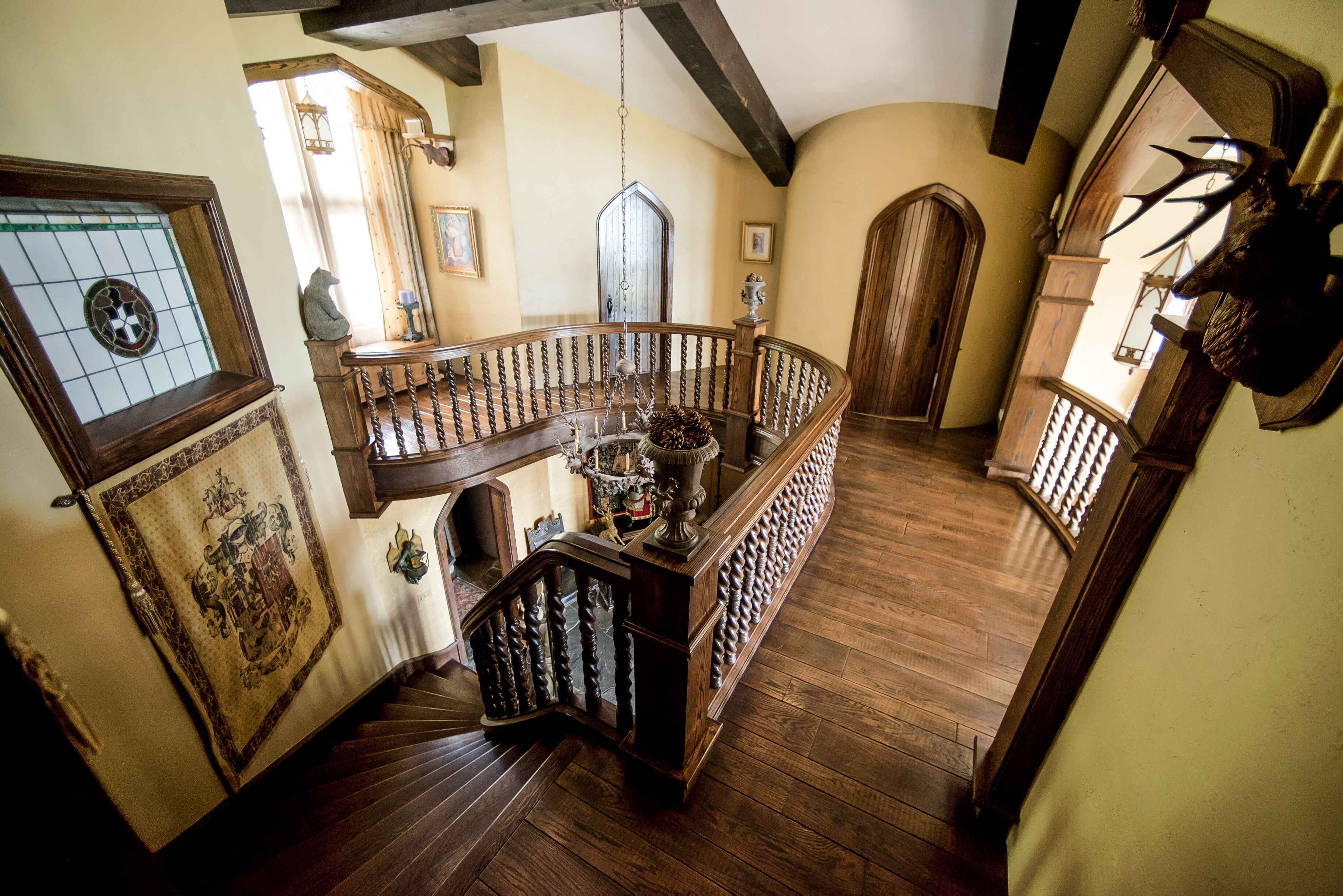 Una gran escalera con barandilla de madera, un candelabro y un escudo en la pared.