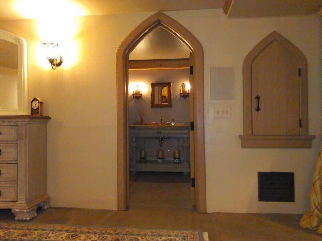 Un couloir menant à une salle de bain avec une porte en bois, un miroir et des appliques murales.