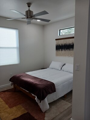 A bedroom with a bed, a ceiling fan, a window, and a wall-mounted macrame piece.