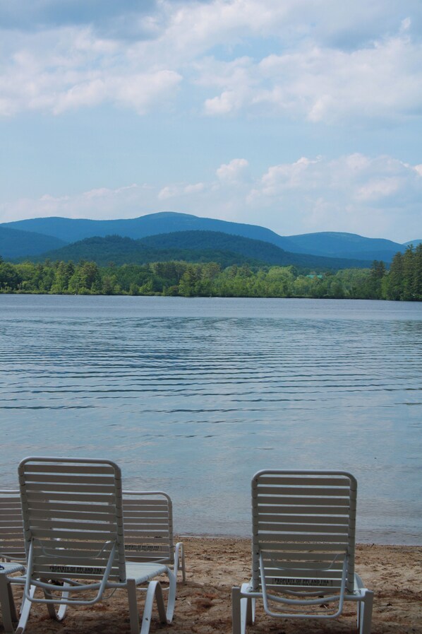 A beach with two metal chairs and a view of a lake and mountains in the background. - Pleasant Point Inn (Lovell)